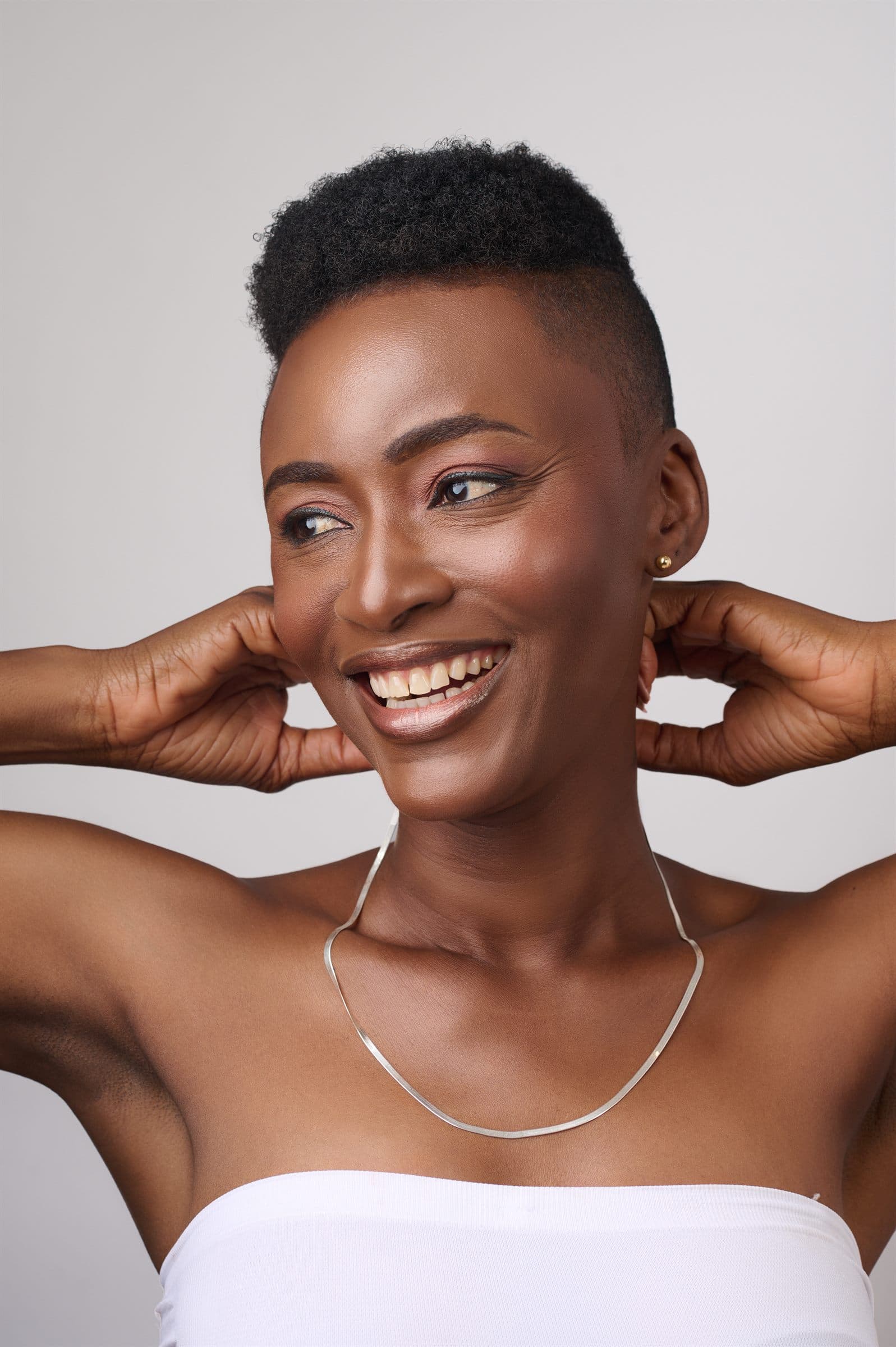 Portrait of a smiling woman, hands framing her face, wearing a fine chain