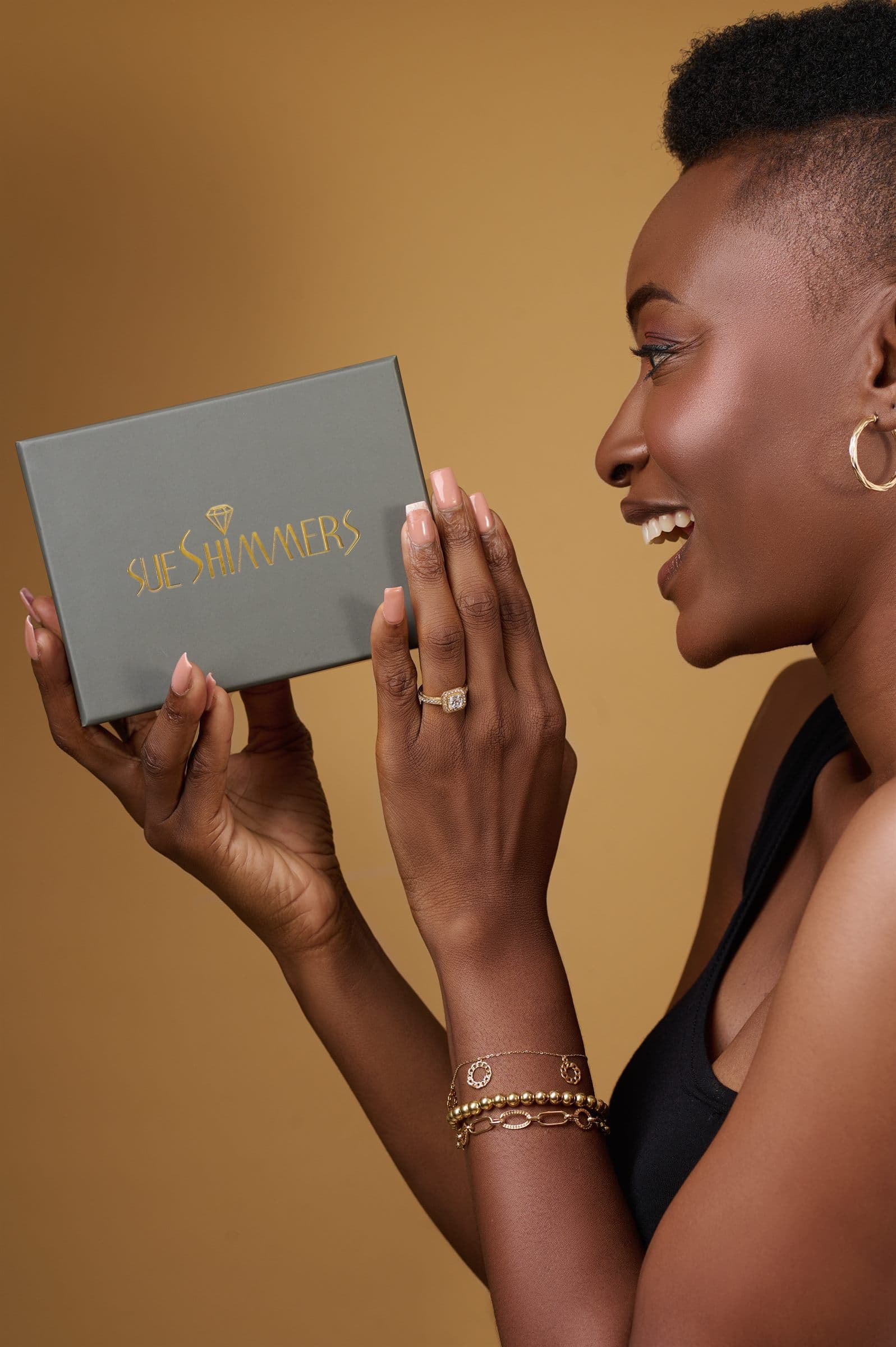 Woman in profile holding a Sue Shimmers box against a tan backdrop