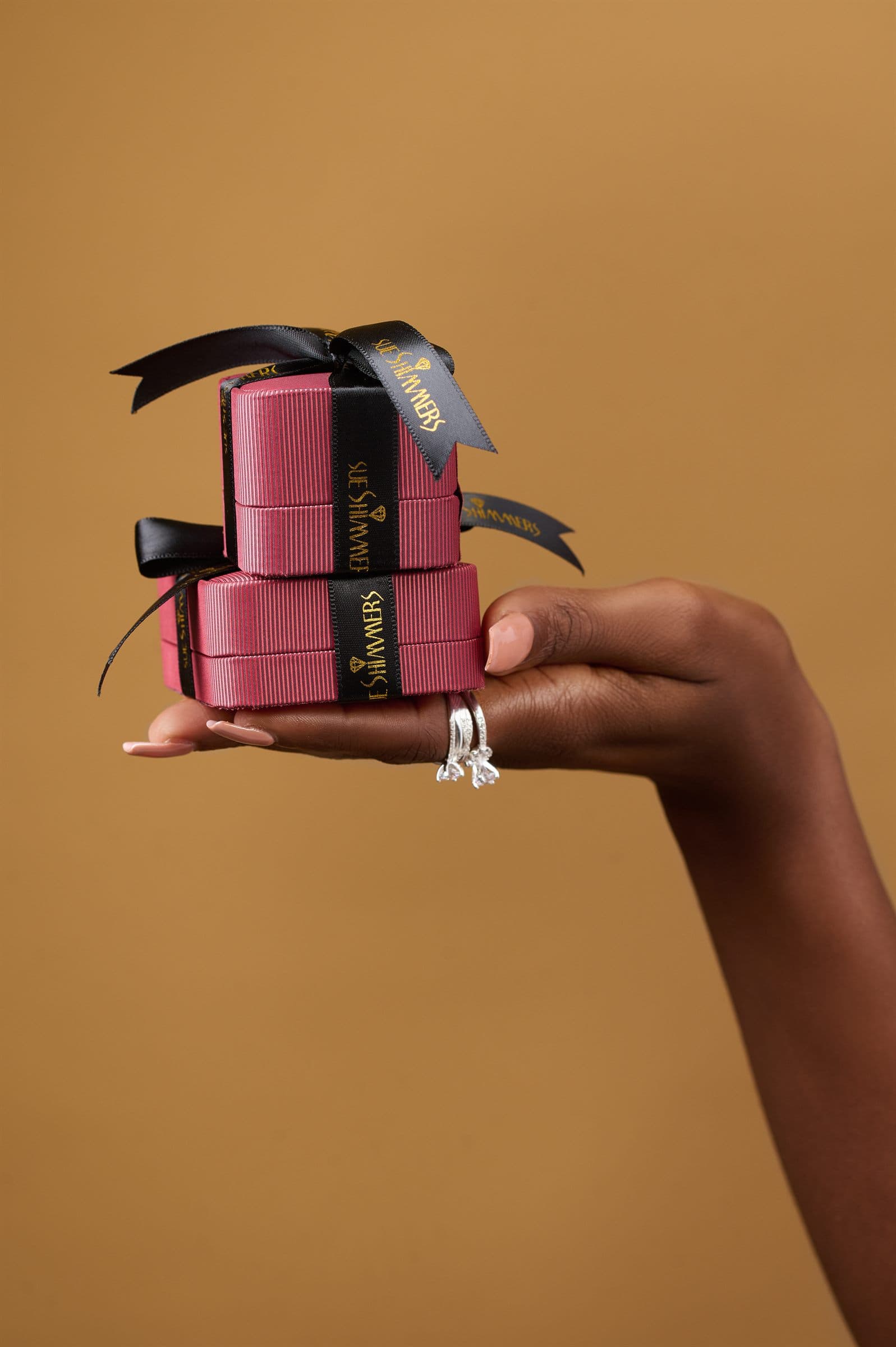Hand with stacked rings holding a tower of ribboned jewelry boxes