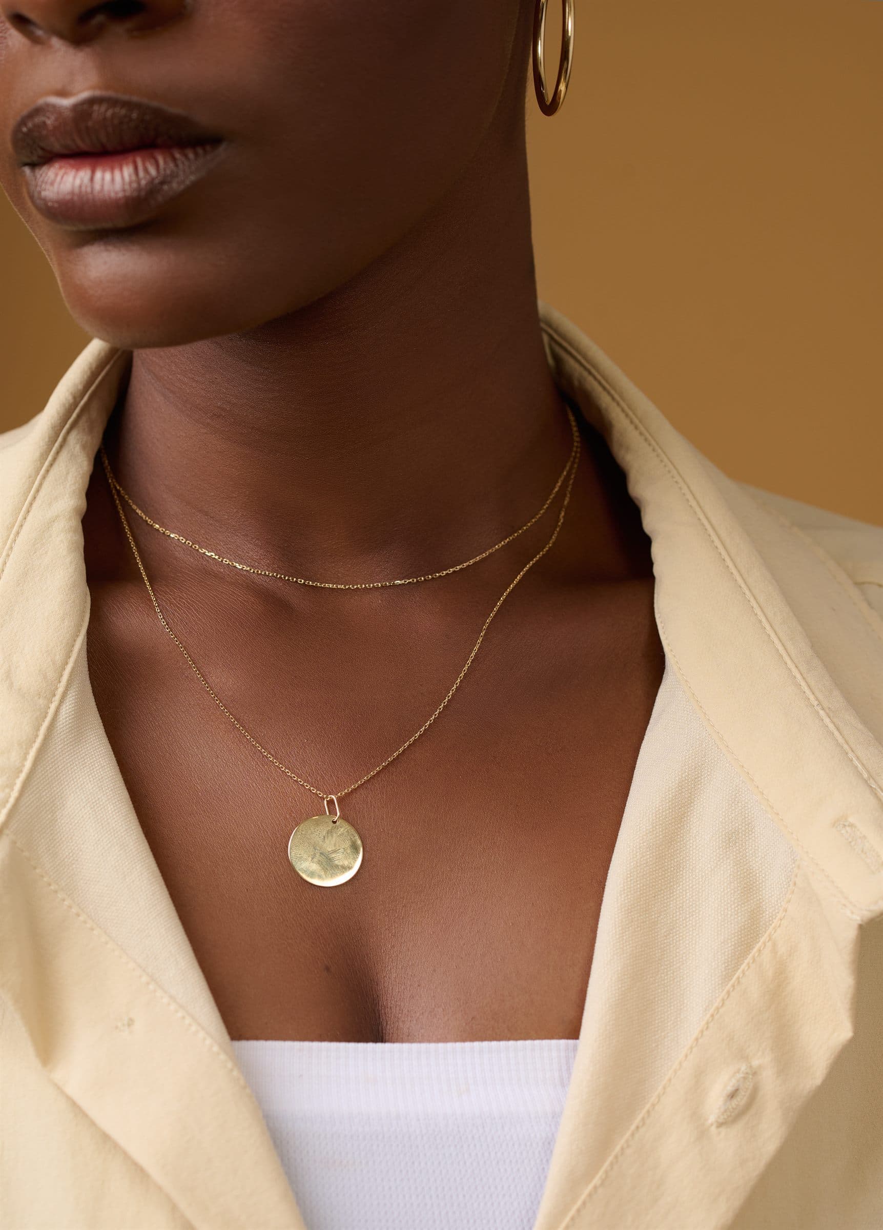 Layered gold coin pendant worn over an open collar