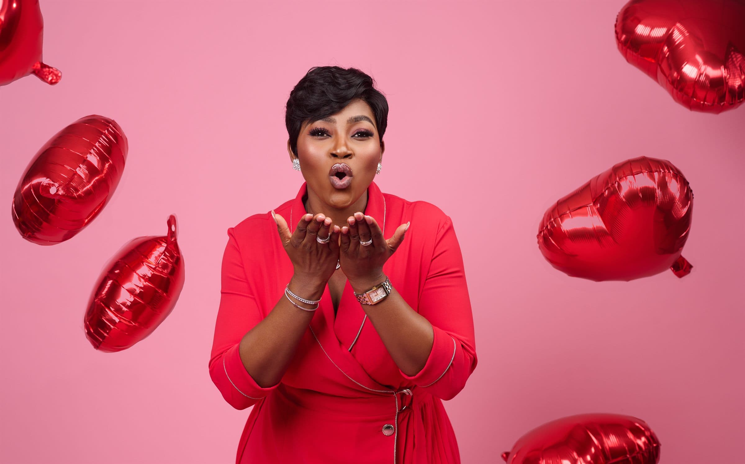 Woman in red blowing a kiss amid falling heart balloons