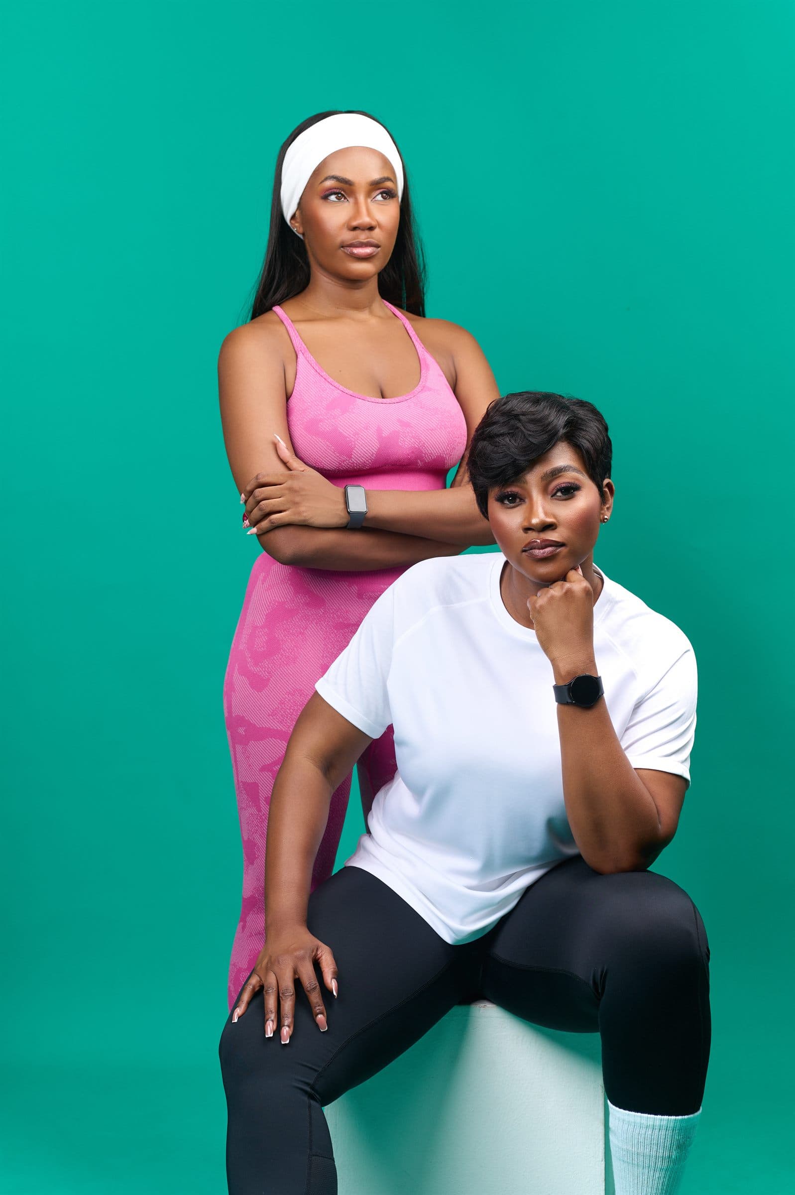 Two women against a teal backdrop, one seated