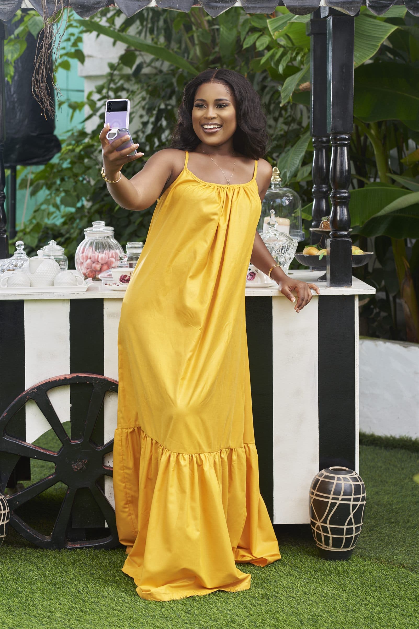 Woman in a yellow dress photographing with a phone in a garden set