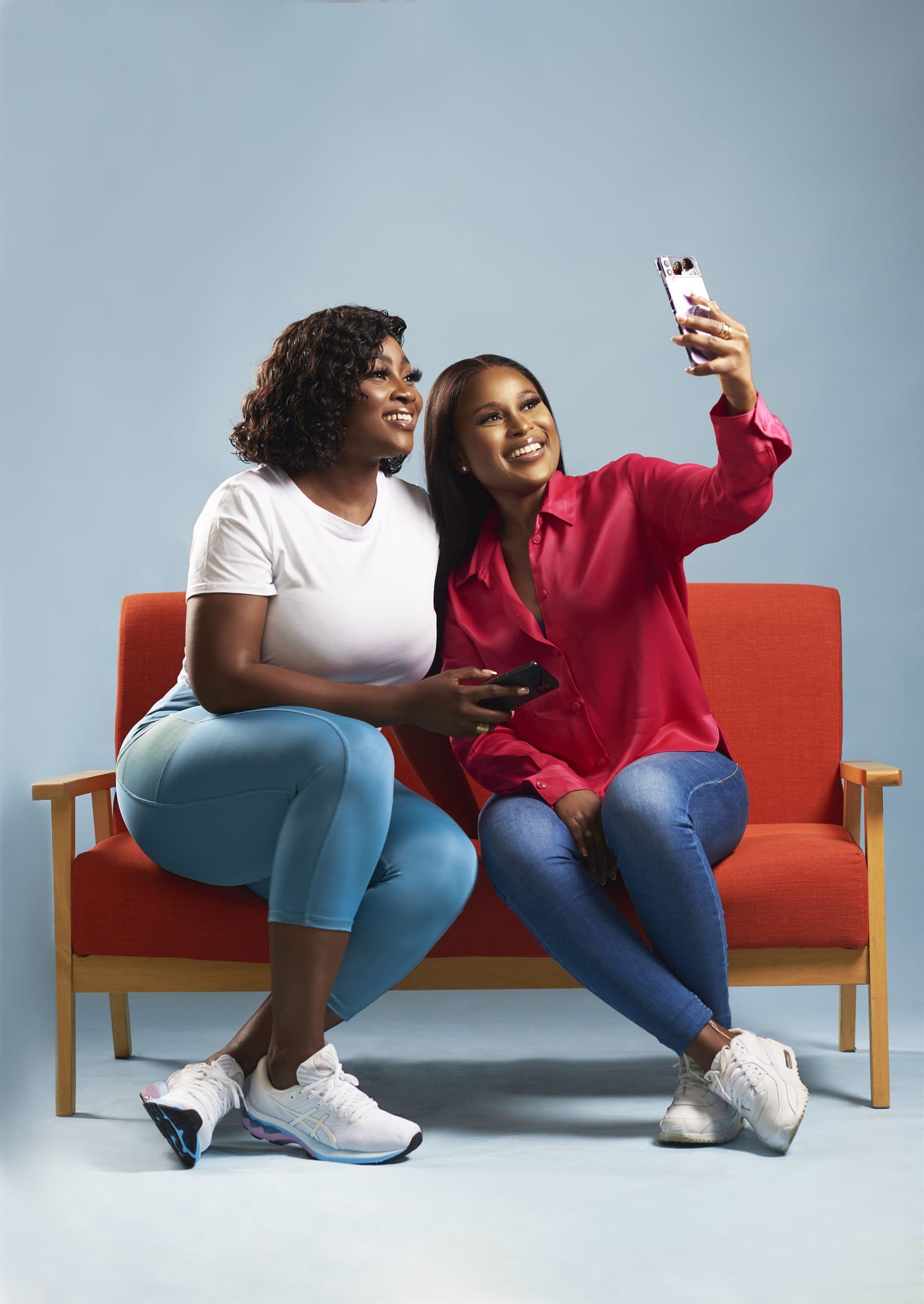 Two friends on a red sofa taking a selfie together