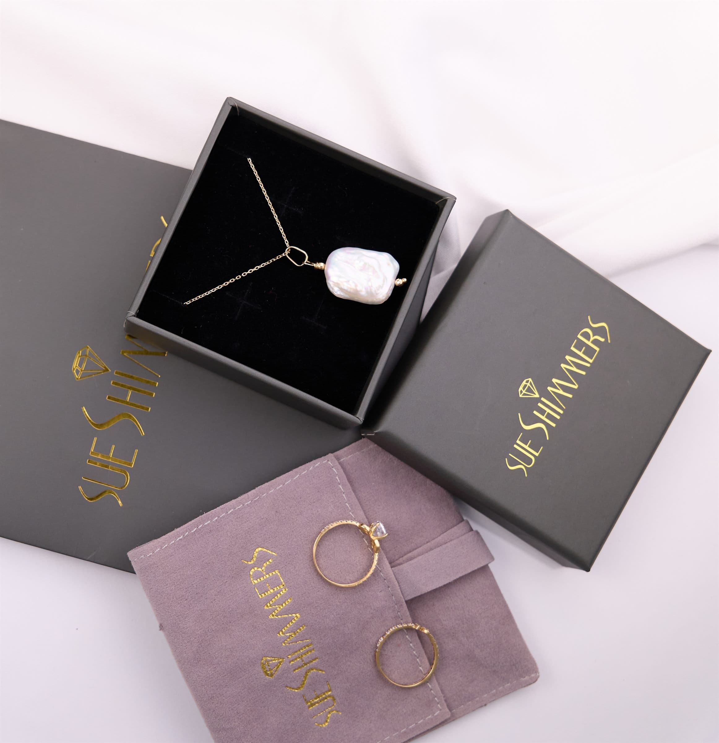 Pendant necklace in an open box beside branded jewelry boxes and a pouch