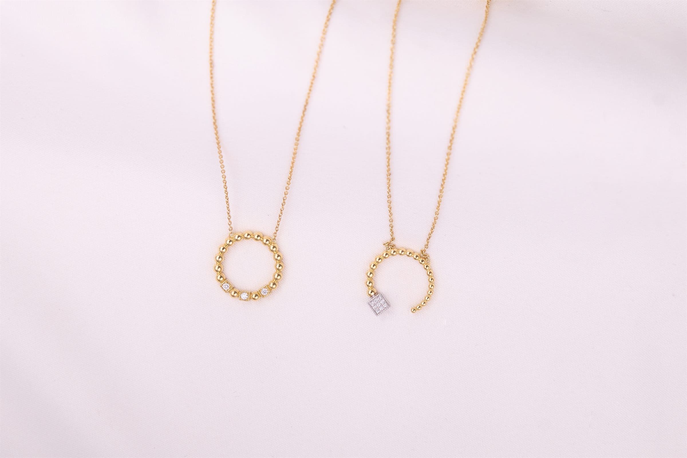 Two gold circle-pendant necklaces on white fabric
