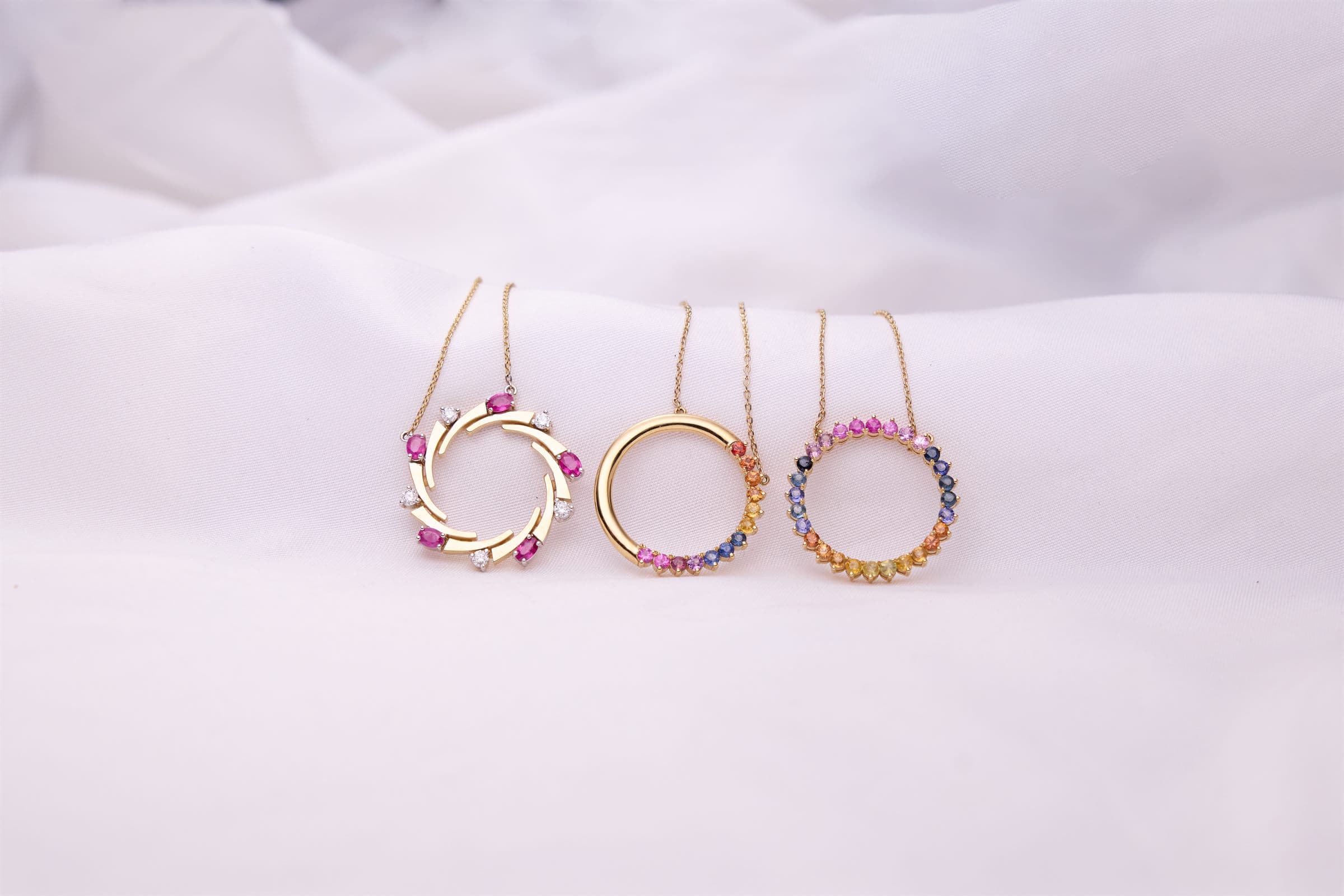 Circle pendants set with coloured gemstones on white fabric
