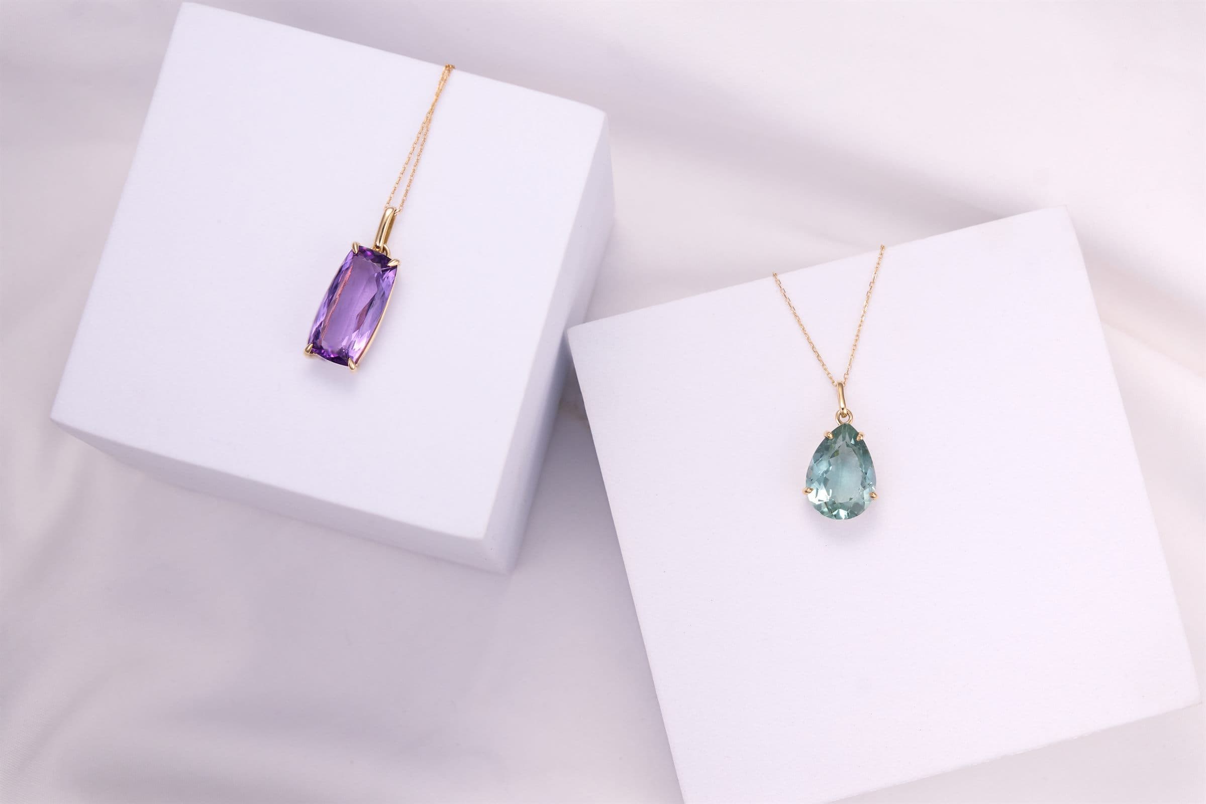 Amethyst and aquamarine pendant necklaces on white blocks