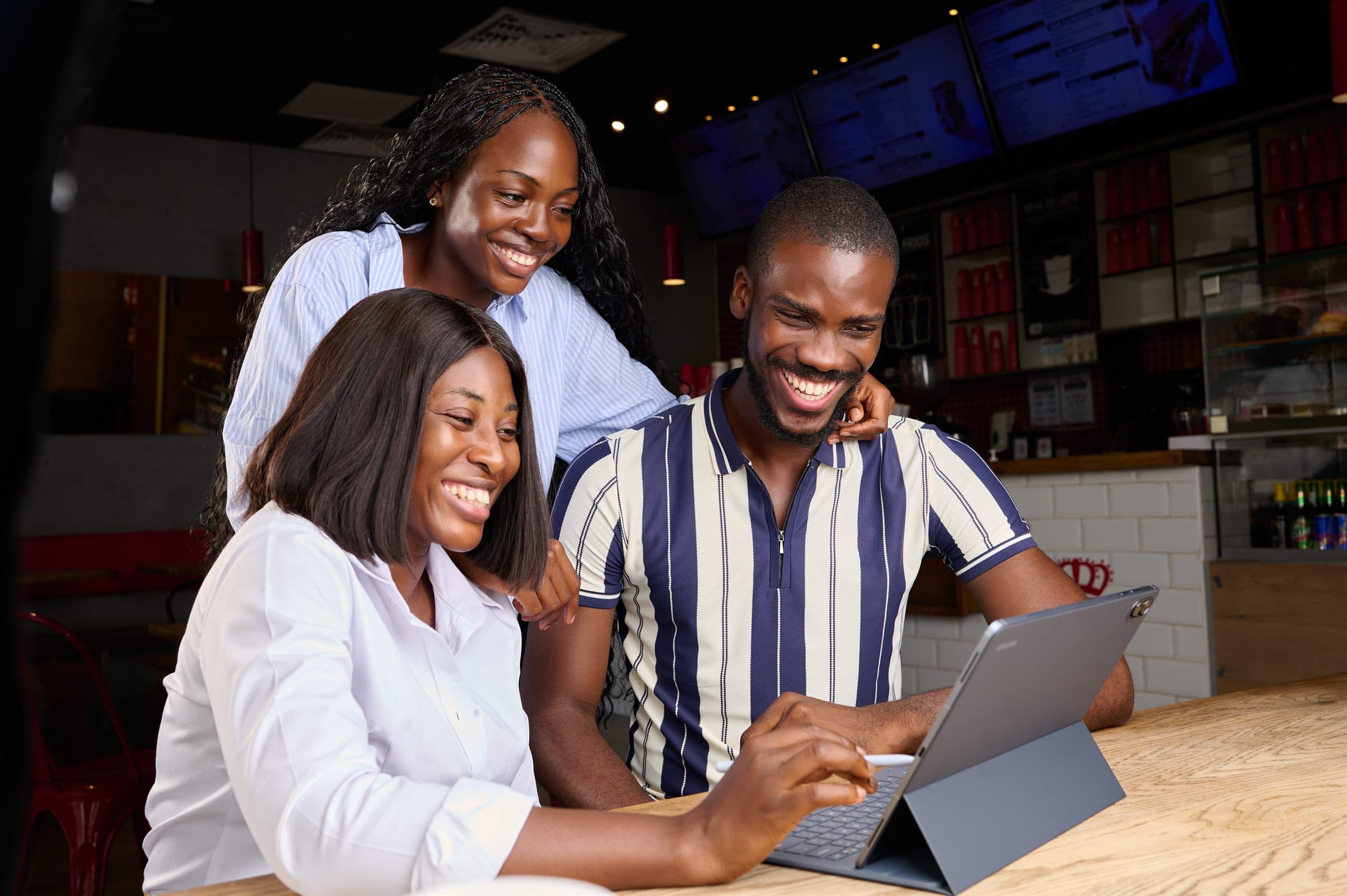 Three colleagues gathered around a tablet at a shop counter